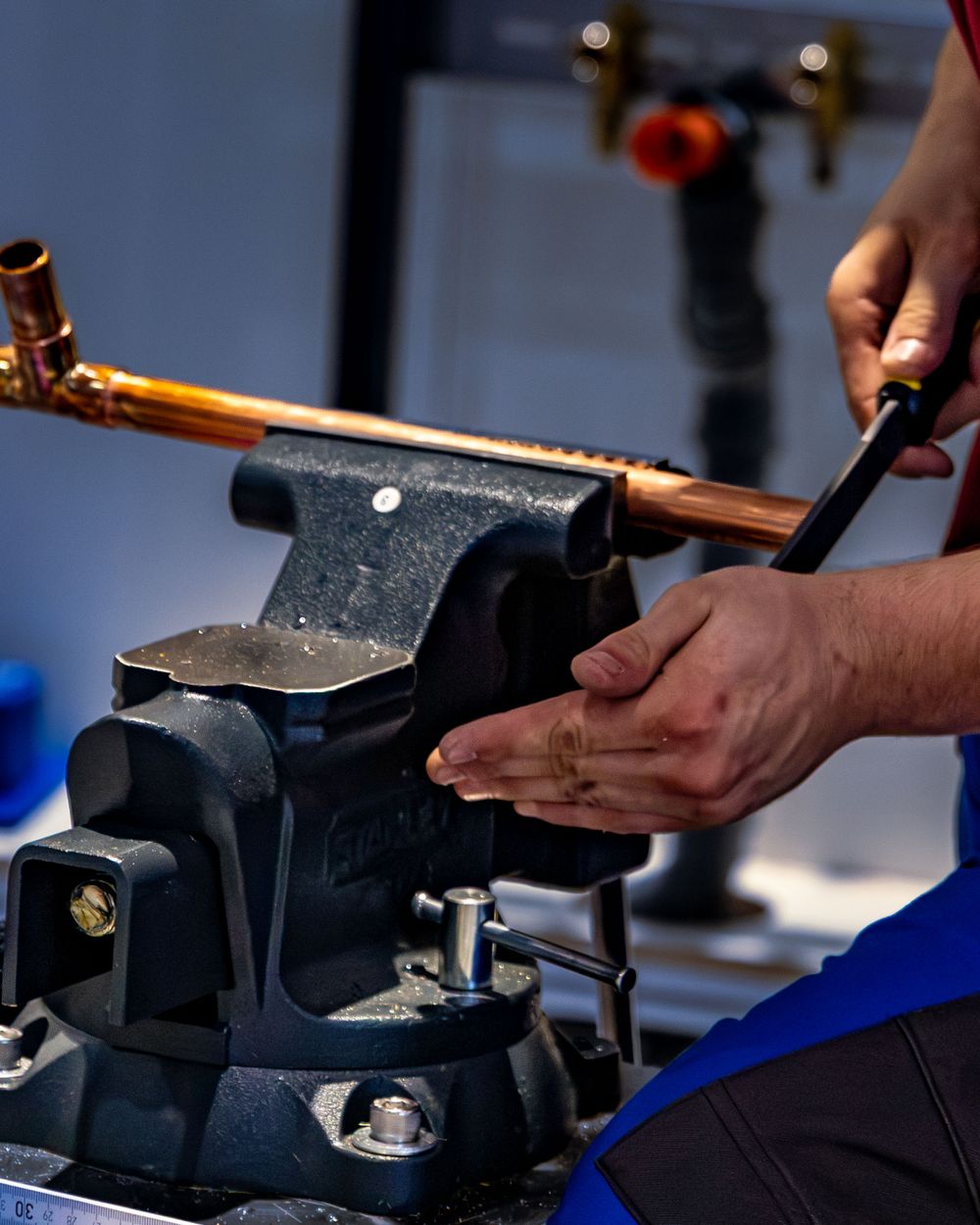 Plumber bending a copper pipe with a pipe bender in a workshop