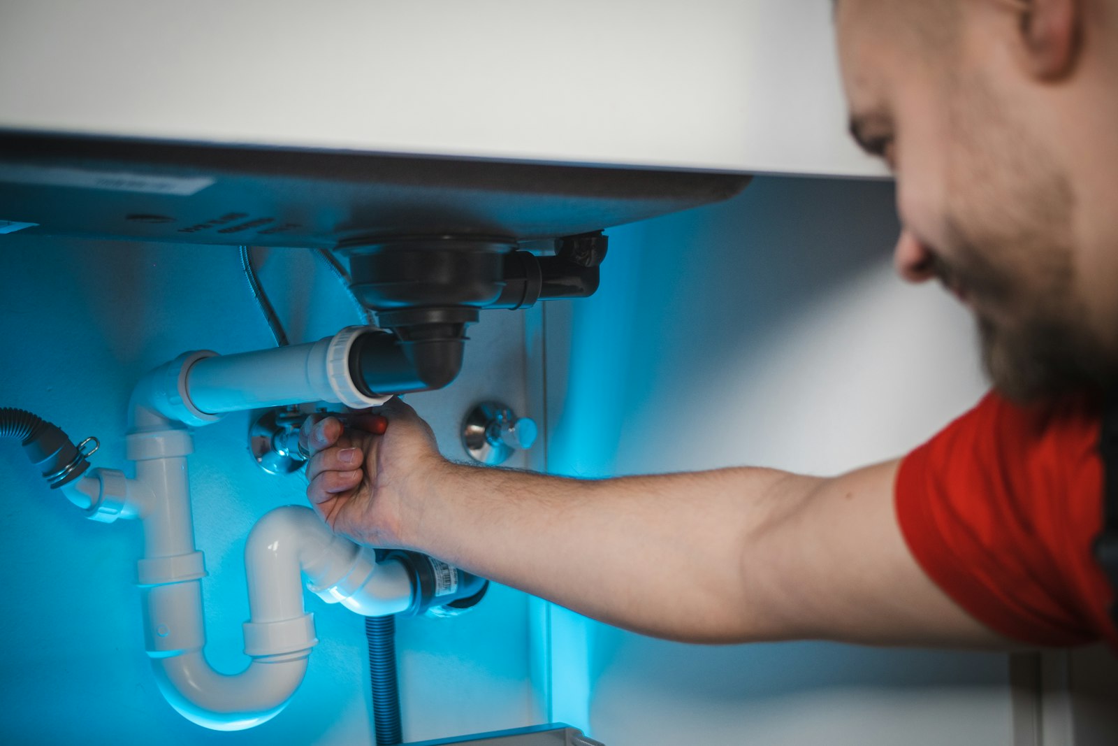 Plumber's hand loosening the drain trap under a bathroom sink