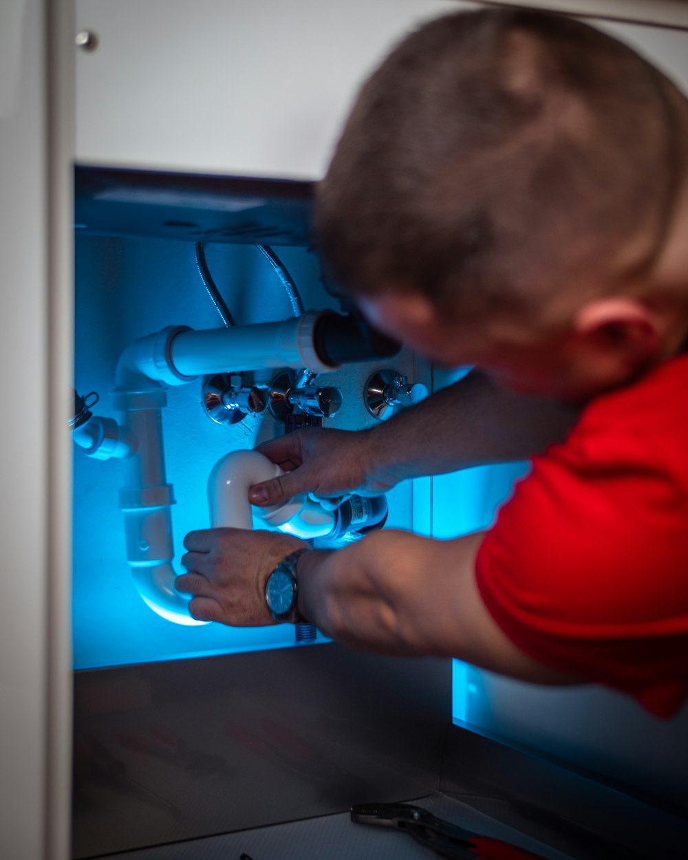 Plumber repairing the drain pipes under a bathroom sink cabinet