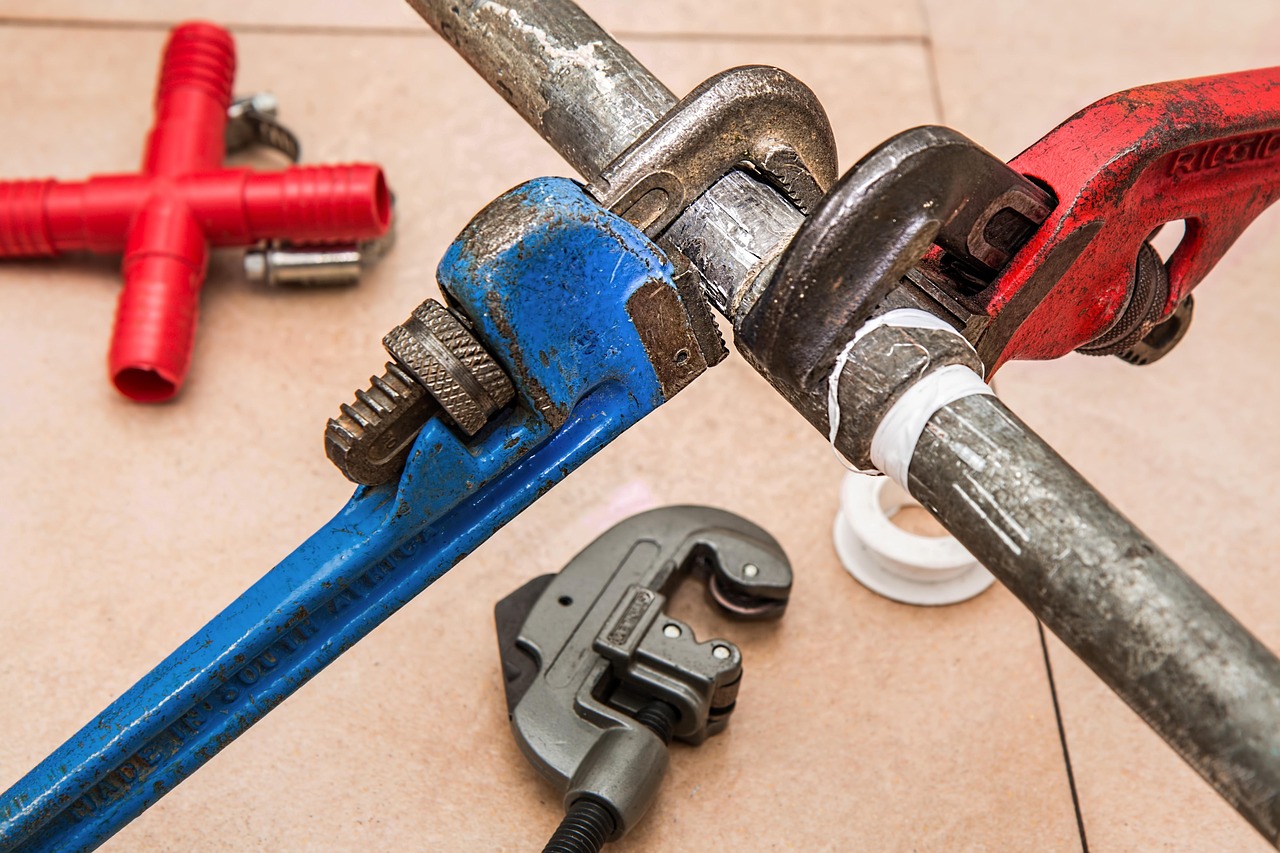 Pipe wrenches, a pipe cutter and thread tape laid out for a plumbing job