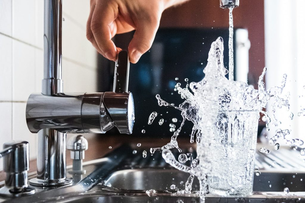 Water running from an open kitchen tap into a stainless steel sink