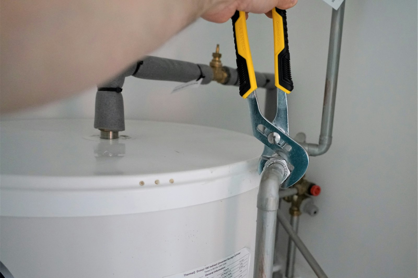 Technician tightening a water heater supply pipe with adjustable pliers