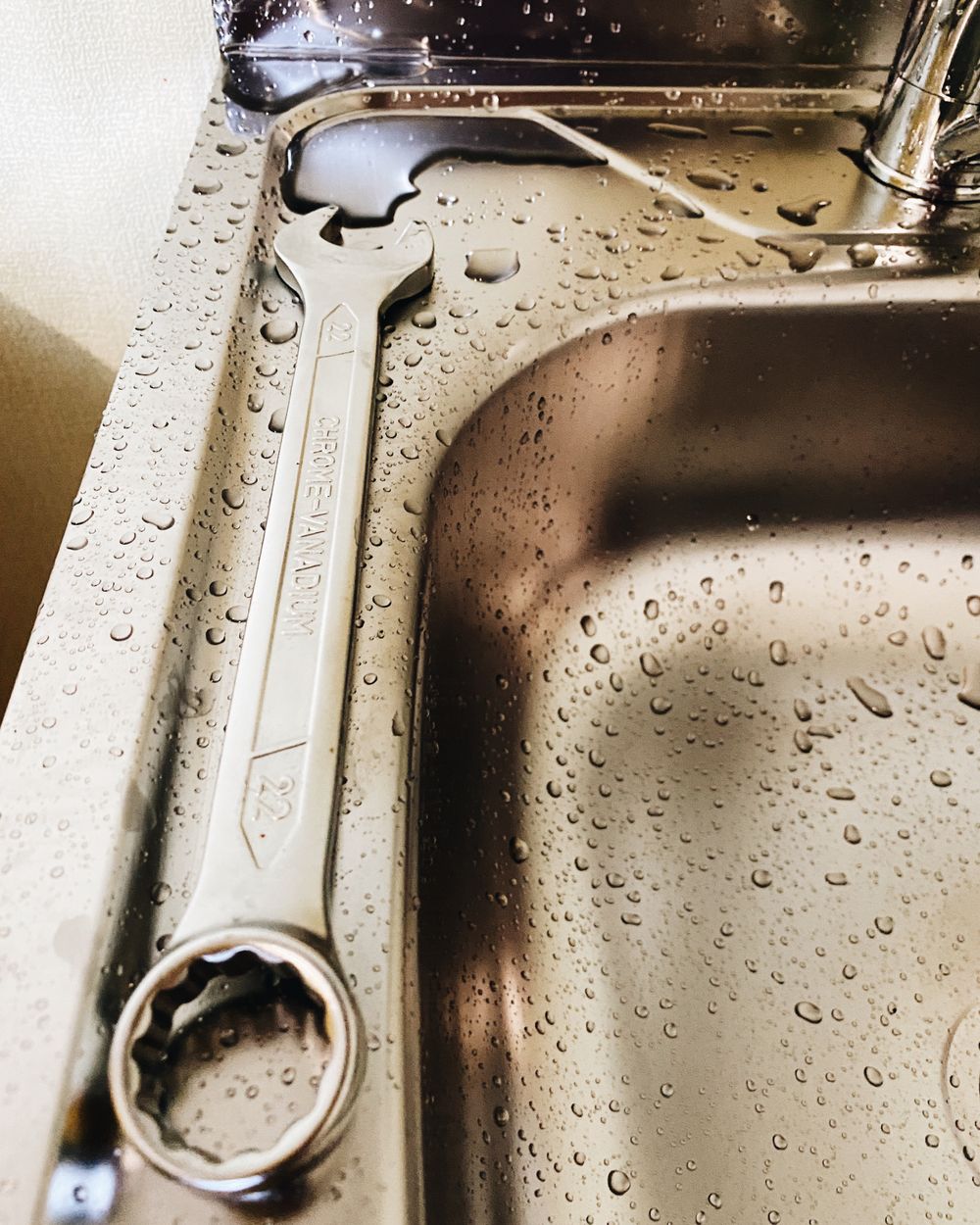 Pipe wrench resting on a stainless steel sink with water droplets